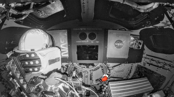 Scientific illustration: a B&W image of the interior of a spacecraft and an astronaut, with a small, orange item floating in midair off to the middle right - a tiny Snoopy doll used to measure relative weightlessness inside the cabin.
