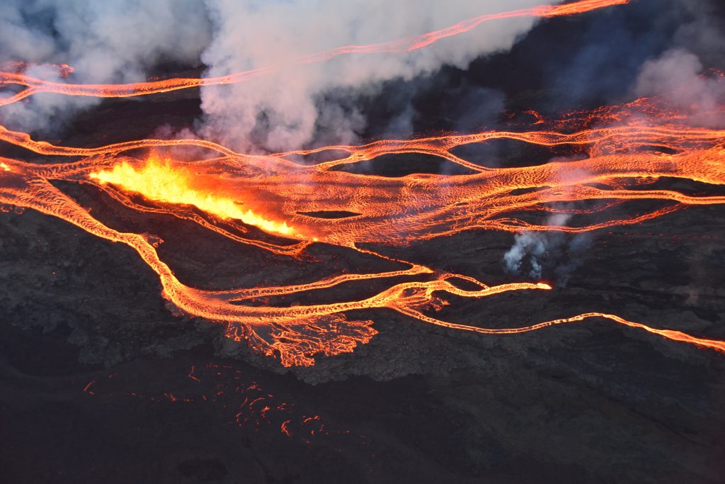 An aerial photo of flowing streams of lava, steam and smoke rising above the black stone and glowing orange lava. Photo from the USGS Hawaiian Volcano Observatory, taken by the Civil Air Patrol.