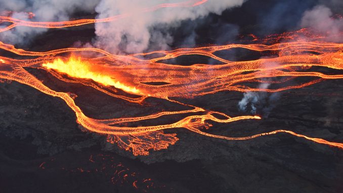 An aerial photo of flowing streams of lava, steam and smoke rising above the black stone and glowing orange lava. Photo from the USGS Hawaiian Volcano Observatory, taken by the Civil Air Patrol.