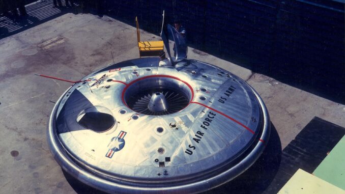 Scientific illustration of an Avrocar, a silver, disc-shaped aerial vehicle, gleaming steel and black vents, parked outside a shaded hangar.