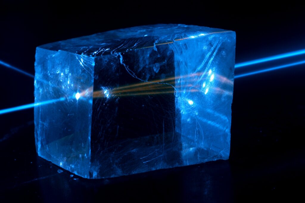 Scientific illustration by Jan Pavelka showing a blue laser creating a fluorescent glow inside a cube of calcite.
