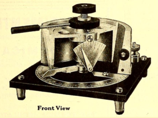 Scientific illustration of an electronic object that looks a little licke a pressure cooker with a cutaway side and some sort of an inditcator needle on the front. It's resting on a square stand with four tiny legs.