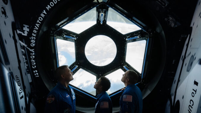 Scientific illustration of astronauts inside a replica of the International Space Station, a hexagonal window looking down on the Earth.