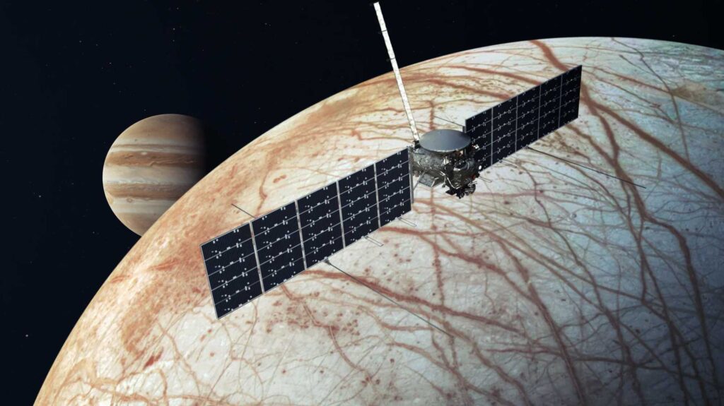 Scientific illustration of the Europa Clipper project, a satellite with long, rectangular solar-dell "wings" over the cris-crossed icy surface of Europa, the frozen moon of Jupiter.