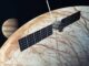 Scientific illustration of the Europa Clipper project, a satellite with long, rectangular solar-dell "wings" over the cris-crossed icy surface of Europa, the frozen moon of Jupiter.