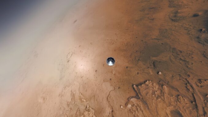 Scientific illustration in the form of an amplified photograph. The frame is filled mostly - but not entirely - with the red surface of Mars, a corner of deep space visible to the top left. In the center, barely visible, is a gleaming steel circle, a tiny droplet of metal descending to the rust-colored surface.