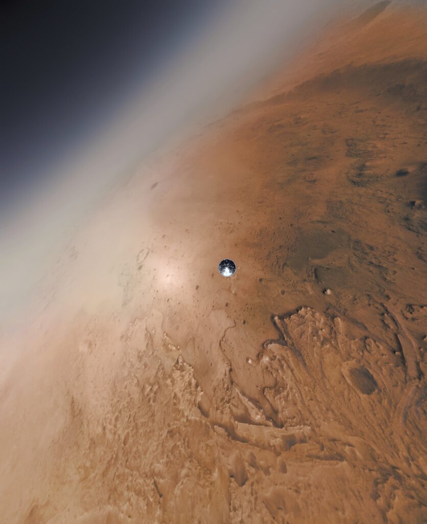 Scientific illustration in the form of an amplified photograph. The frame is filled mostly - but not entirely - with the red surface of Mars, a corner of deep space visible to the top left. In the center, barely visible, is a gleaming steel circle, a tiny droplet of metal descending to the rust-colored surface.