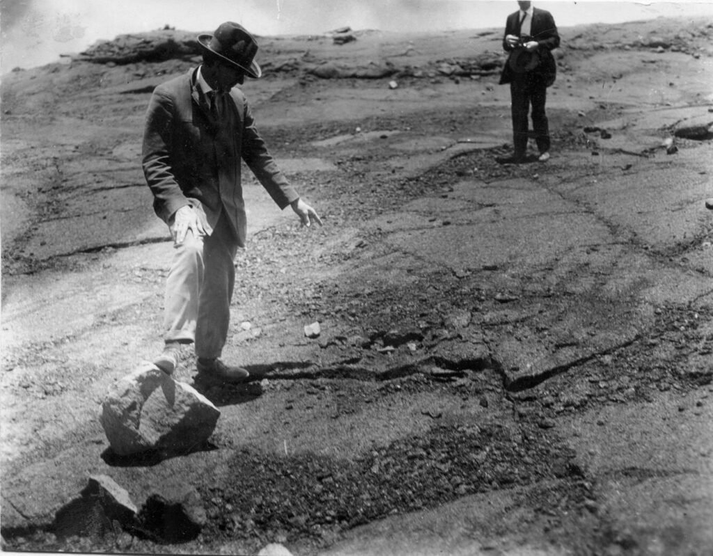 Scientific illustration of the aftermath of a volcanic eruption, with a man in a suit standing beside a large rock, apparently holding his arms out for scale. Such was science in 1925.
