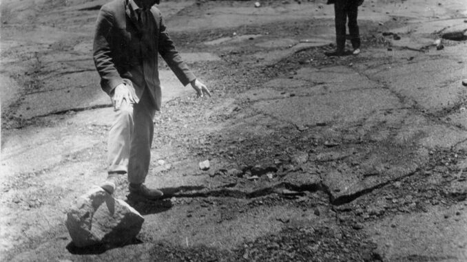 Scientific illustration of the aftermath of a volcanic eruption, with a man in a suit standing beside a large rock, apparently holding his arms out for scale. Such was science in 1925.