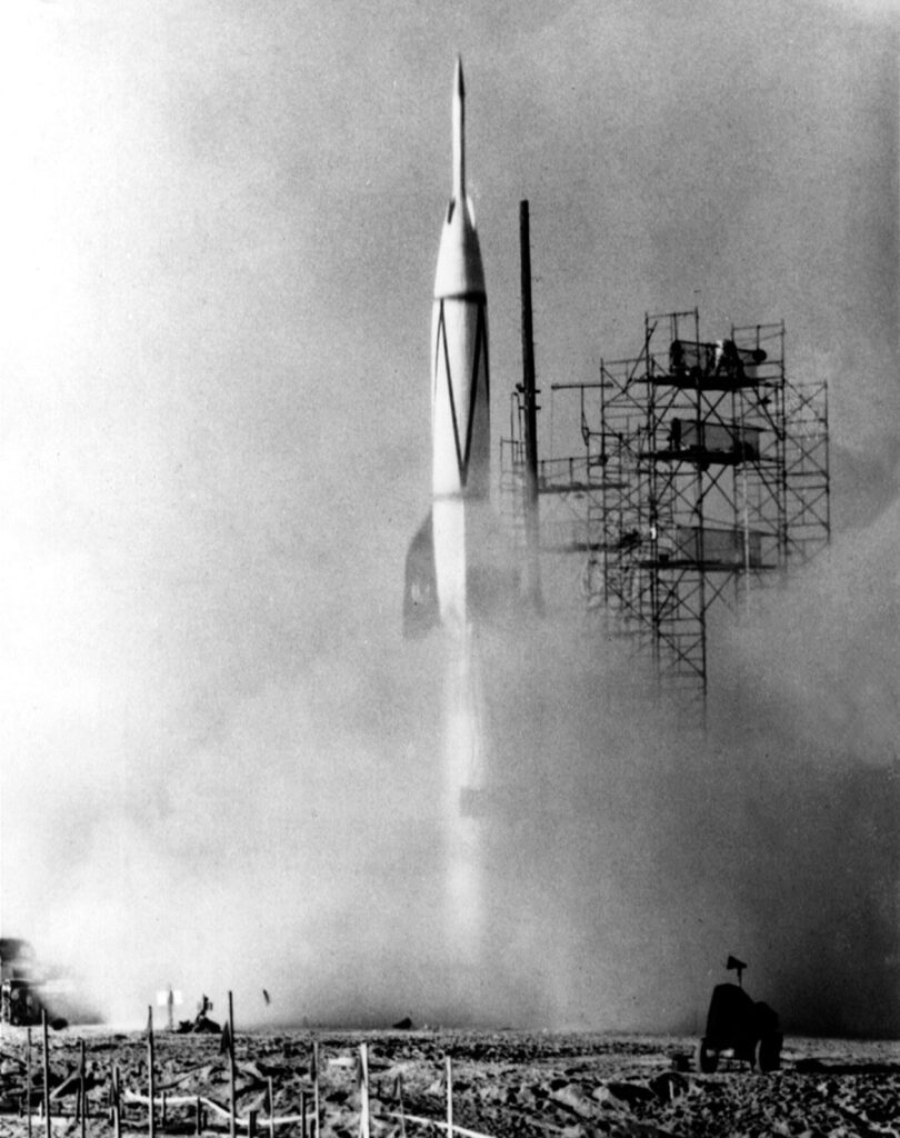 Scientific illustration of a rocket launching in the 1950s, metal scaffolding and exhaust clouds, a white tower rising skyward, gleaming in black and white.