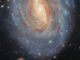 Scientific illustration of a spiral galaxy snapped by a space telescope, a yellow and blue spiral whirling against the blackness of space, with a bonus image of an asteroid moving much closer to Earth off to the right side, visible as four thin, colored lines: snapped when the telescope took four different colored exposures.